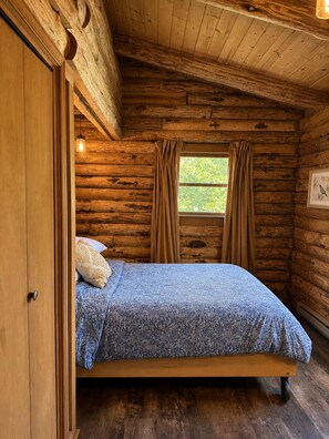 A wooden cabin room with a bed, curtains, and a window.