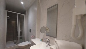 Un baño moderno con cabina de ducha de vidrio, inodoro, lavamanos y espejo.