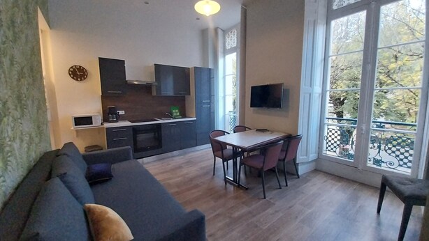 Un espacio habitable moderno con sofá, mesa de comedor, sillas, zona de cocina y ventanas amplias.