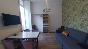 Una sala de estar con televisor, una mesa de comedor con sillas, un sofá y un papel tapiz estampado.