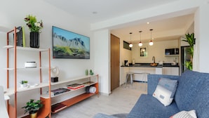 Een moderne woonkamer met een bank, een boekenkast en een flatscreen televisie. In de achtergrond is een keuken te zien.