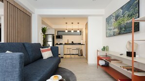 A modern living room with a sofa, a coffee table, and a bookshelf. A kitchen is visible in the background.