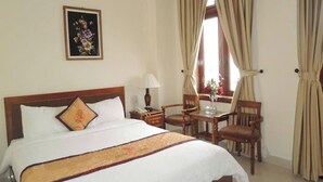 Ein Hotelzimmer mit Bett, Schreibtisch, Stühlen, einem Fenster mit Vorhängen und einem Wandbild.