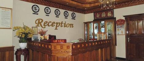 A reception area with a wooden reception desk, a chandelier, and clocks indicating different cities.