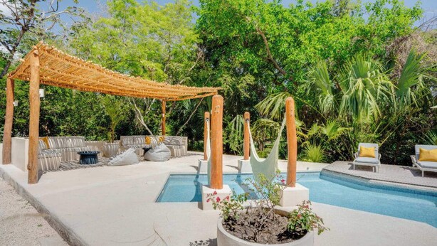 Ein Poolbereich mit einer Pergola, Liegestühlen und einem kleinen Garten.