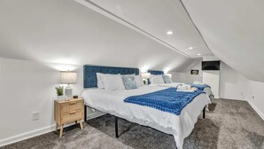 Ein modernes Schlafzimmer mit zwei Betten, einer blauen Kopfteil, weißer Bettwäsche, einem Nachttisch mit Lampe und einer kleinen Pflanze.