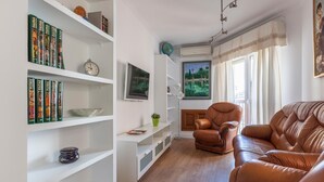 Ein Wohnzimmer mit braunem Ledersofa, weißen Regalen mit Büchern, einer Uhr und einem Gemälde.