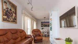 Ein Wohnzimmer mit braunem Ledersofa, einem Esstisch mit Stühlen, einem weißen Schrank und einem Bild an der Wand.