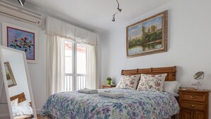 Ein Schlafzimmer mit einem hölzernen Bett, blumigem Bettzeug, einem Nachttisch mit Lampe und einem Gemälde an der Wand.