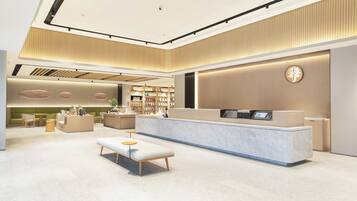A modern hotel lobby with a reception desk, seating area, and a large bookshelf.