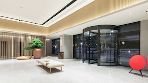 Eine moderne Lobby mit einem runden roten Sessel, einem Blumentopf und einem Glaselevator.