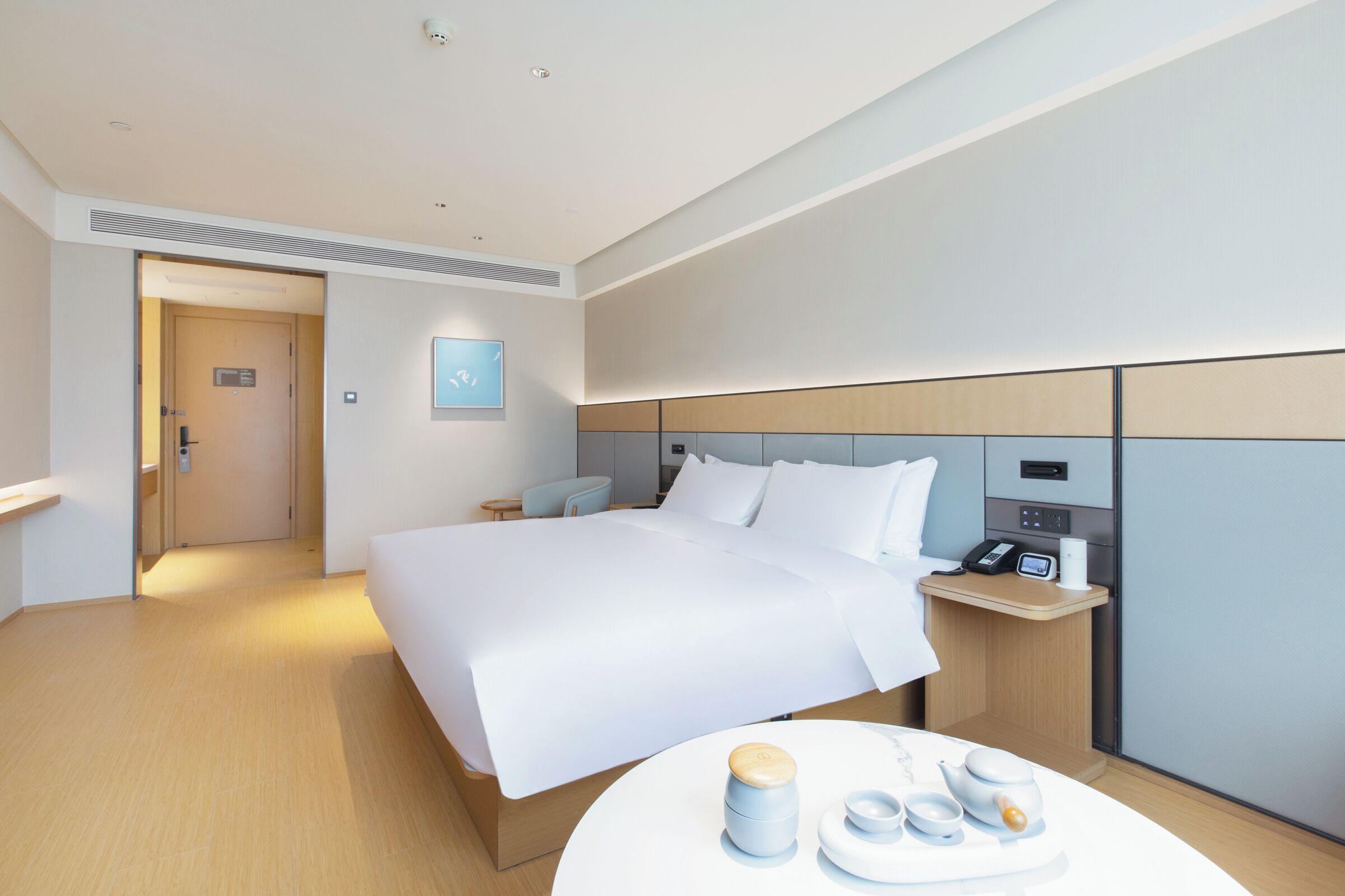 Una habitació d'hotel moderna amb un llit gran, una taula de nit i una taula rodona petita amb una bandeja de te i caragols de llet.