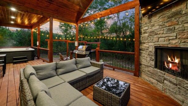 Une terrasse extérieure avec une cheminée en pierre, un canapé et un jacuzzi.