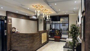 Un mostrador de recepción con detalles de madera, un área de recepción con piso de mármol y un ventanal que ofrece vistas del interior.