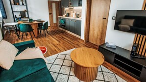 Een moderne woonkamer met een groene bank, een houten salontafel en een tv-meubel met een flatscreen televisie.