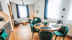 Een moderne woonkamer met een ronde houten tafel, groene fluweelstoelen en een blauwe bank.