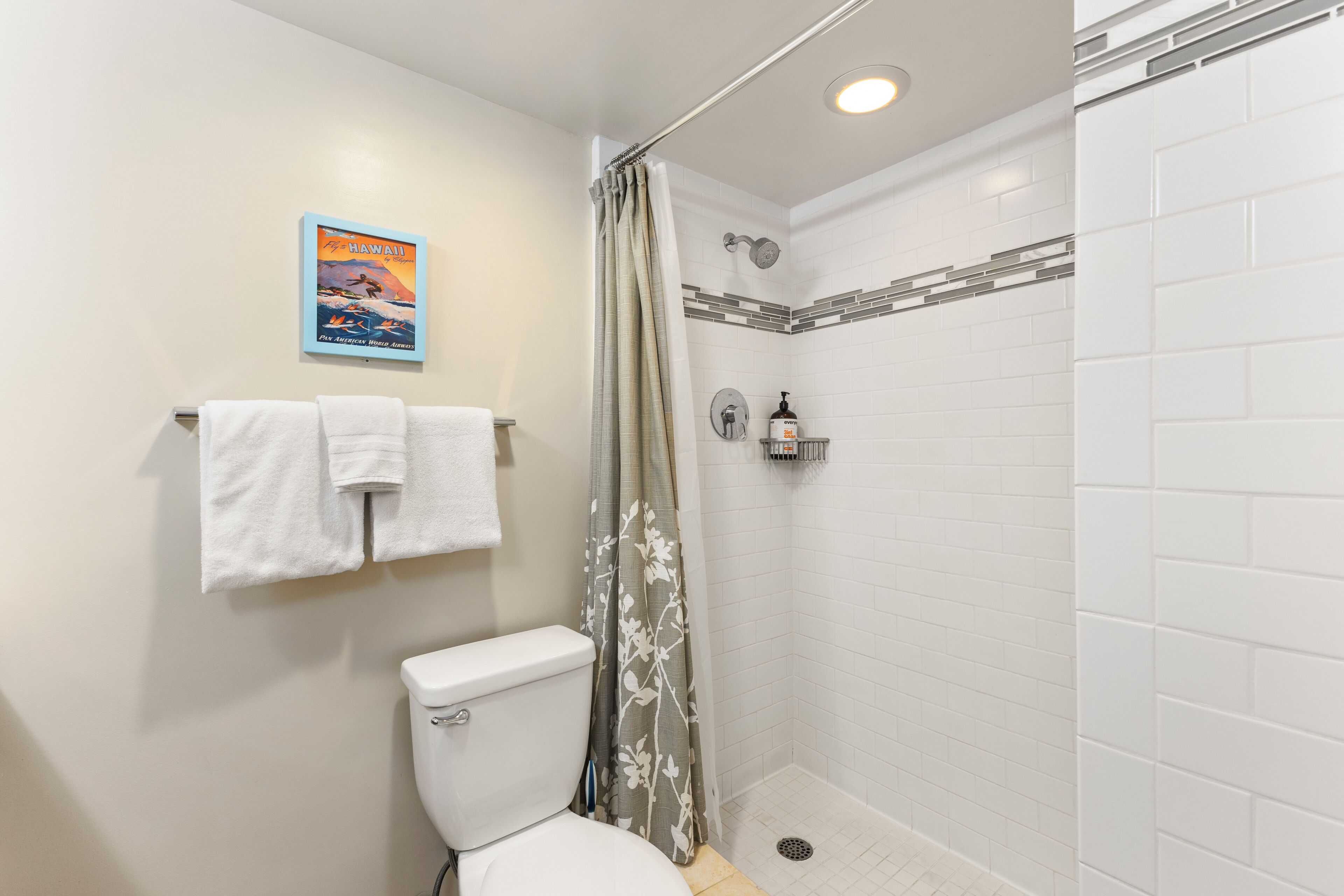 Un baño con inodoro, ducha con puerta de vidrio, paredes de azulejos blancos y un cartel en la pared.