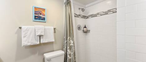 Un baño con inodoro, ducha con puerta de vidrio, paredes de azulejos blancos y un cartel en la pared.