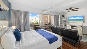 A modern hotel room with a large bed, a seating area with a sofa and armchairs, a TV, and a balcony with a city view. - Ilikai Hotel Studio (Honolulu)