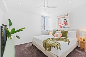 Un dormitorio moderno con una cama grande, un ventilador de techo, una ventana con persianas y un cuadro en la pared.