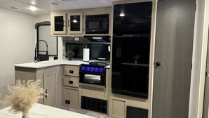 Une cuisine compacte dotée d’appareils électroménagers intégrés, d’un four à micro-ondes, d’une cuisinière et d’un évier.