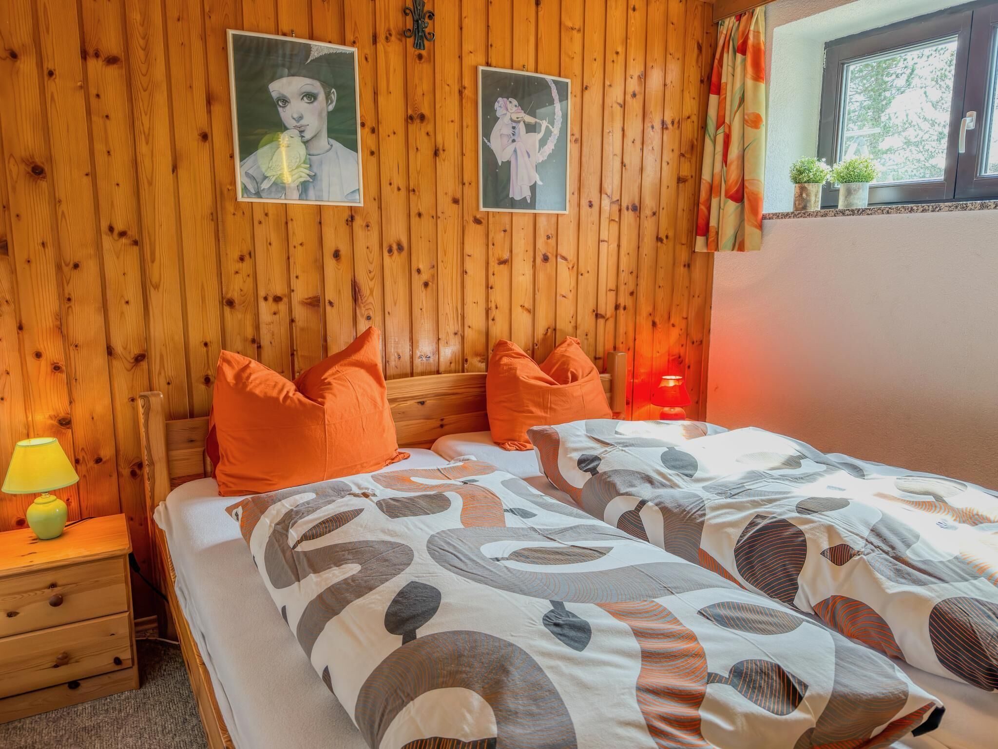 Une chambre avec un mur lambrissé en bois, deux lits avec des oreillers orange, une table de chevet avec une lampe et deux tableaux encadrés.