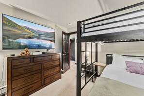 A bedroom with a bunk bed, a wooden dresser, a flat-screen TV, and a large window with a scenic view.