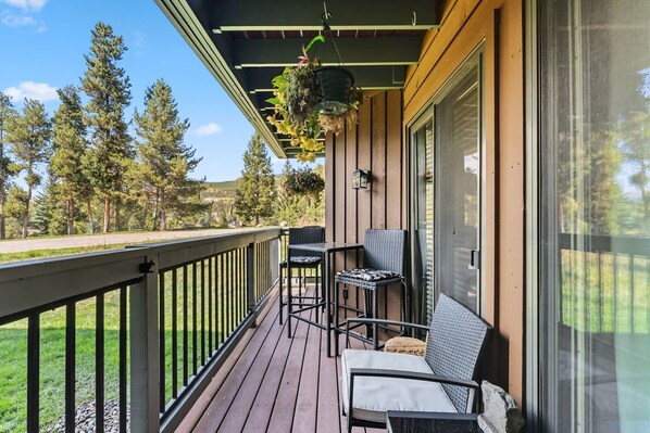 A wooden deck with outdoor furniture, a hanging planter, and a view of trees and a road.