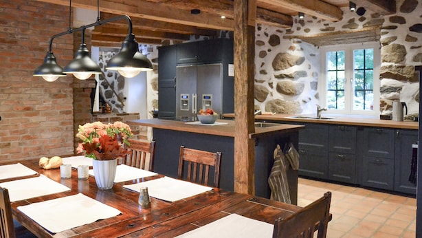 A rustic kitchen with exposed beams, a stone wall, and a wooden dining table set with placemats and a vase of flowers. - Lovely home in Sallerup with WiFi (Sallerup)