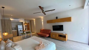 Ein modernes Hotelzimmer mit einem großen Bett, einem Fernseher, einem Deckenventilator und einer Küchenzeile.