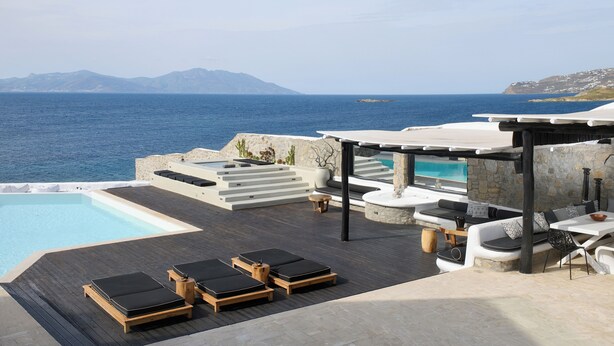 Un área junto a la piscina con sillones de relax, un rincón de estar con cojines y vistas al mar y a las montañas.