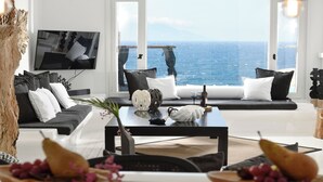 Un salón moderno con un amplio ventanal con vistas al mar, un televisor de pantalla plana montado en la pared y una disposición de mobiliario minimalista.