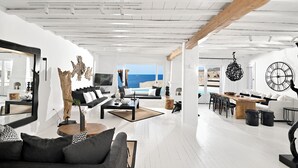 Un salón moderno con decoración blanca, un espejo grande y vista al mar.
