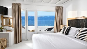 Un dormitorio con una cama grande, televisión, cabecera de madera, ventana con cortinas y vistas al mar.