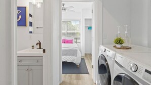 A laundry area with a washing machine, a sink, and a bed with a pink pillow.