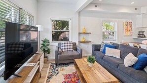 A modern living room with a flat-screen TV, grey sofas, a wooden coffee table, and a colorful rug.