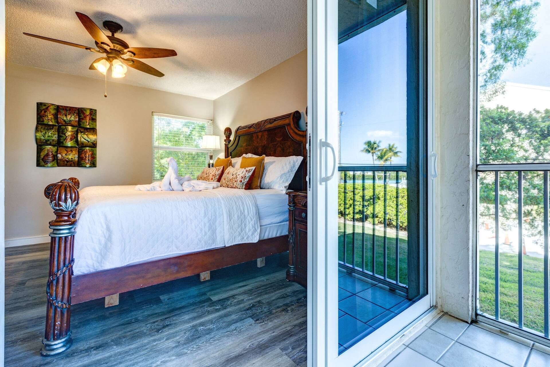 A bedroom with a wooden bed, a ceiling fan, and a view of a balcony with a glass door.