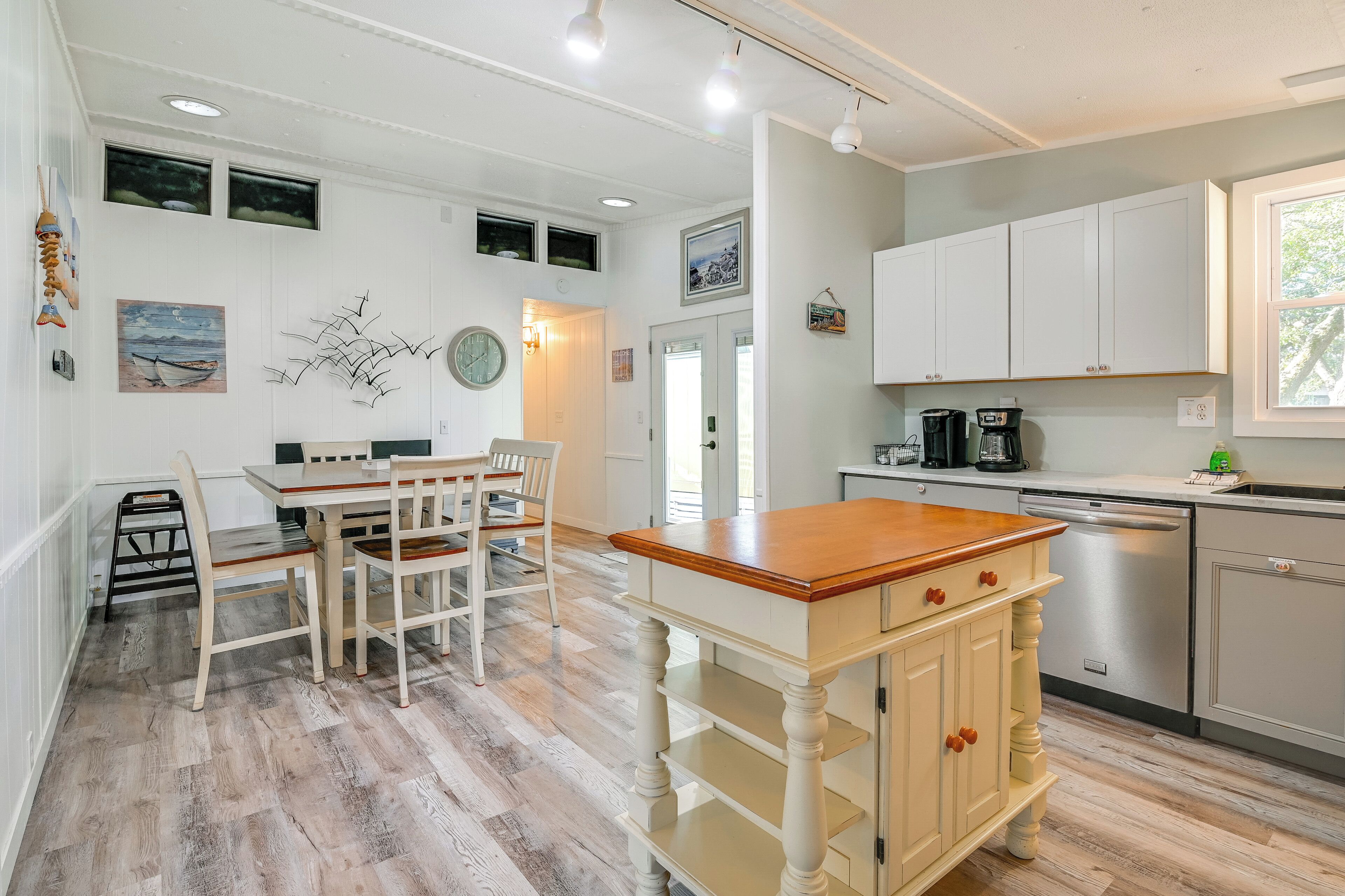 A modern kitchen with white cabinetry, a wooden dining table, and a built-in dishwasher.