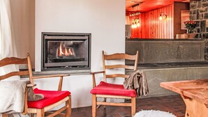 Una habitación acogedora con chimenea, sillas de madera con cojines rojos y una pared de piedra.
