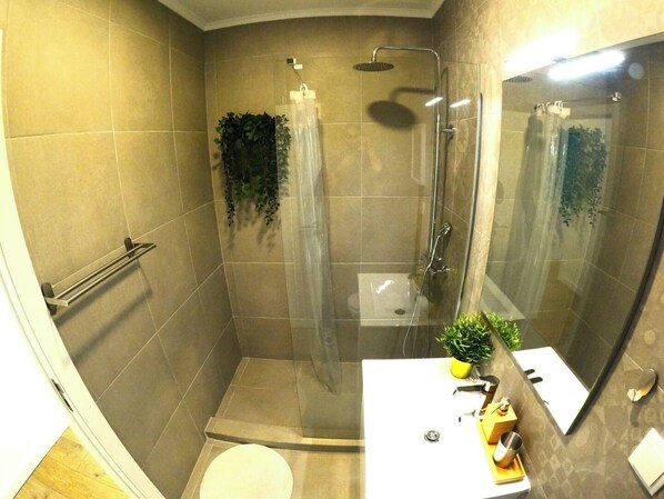 A bathroom with a shower, toilet, sink, and a mirror.