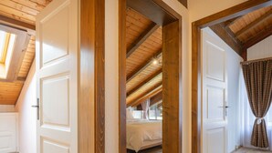 A room with wooden beams, white doors, and a bed with a white bedspread.