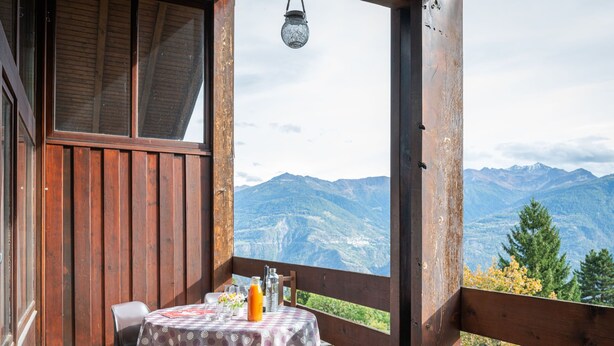 A wooden balcony with a table set for two, overlooking a mountainous landscape.