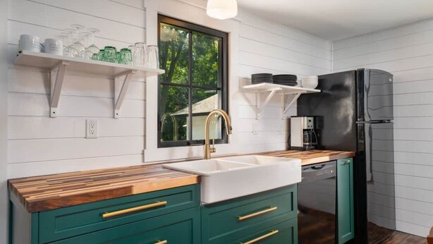 Una cocina con encimera de madera, armarios verdes, un refrigerador negro y una ventana con vistas a la vegetación.