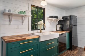 Een keuken met een houten aanrecht, groene kasten, een zwarte koelkast en een raam met uitzicht op groen.