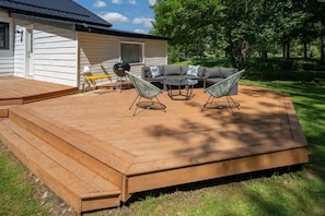 A deck with outdoor furniture, a grill, and a house in the background.