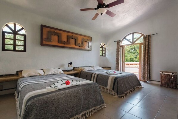 Una habitación con dos camas, ventilador de techo y vista por la ventana.