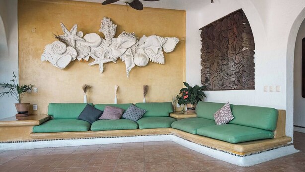 A green sectional sofa with decorative wall art and a ceiling fan in a room with tiled flooring. - Casa Bravo - Garden Oasis Steps from la ropa (Zihuatanejo)