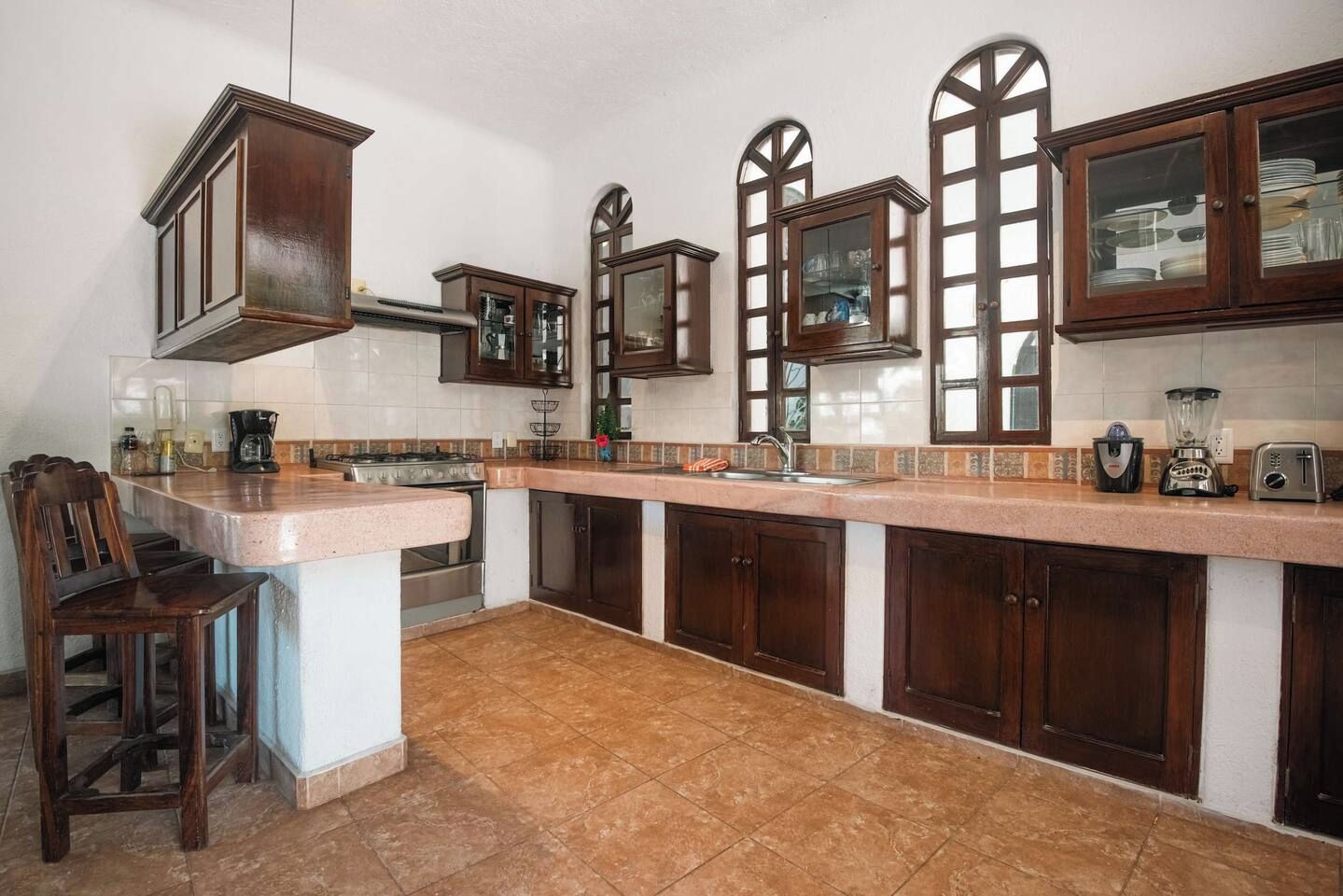 A kitchen with a central island, dark wooden cabinets, a stainless steel stove, and a tiled backsplash.