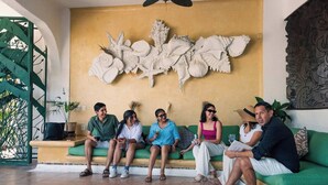A group of people sitting on a green sofa in a room with a decorative wall art piece and a green gate. - Casa Bravo - Garden Oasis Steps from la ropa (Zihuatanejo)