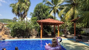 A swimming pool with clear blue water, surrounded by lush greenery and palm trees. - Casa Bravo - Garden Oasis Steps from la ropa (Zihuatanejo)